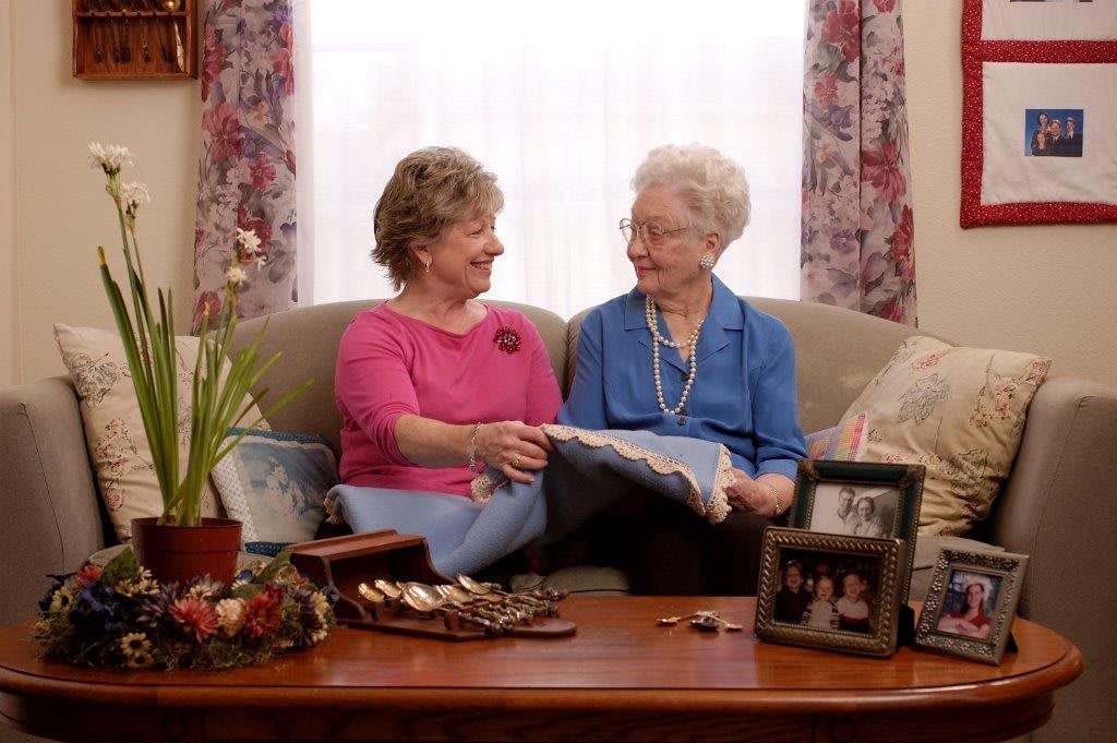 Two women sitting on a sofa, sharing a moment of conversation and laughter in a cozy living room.