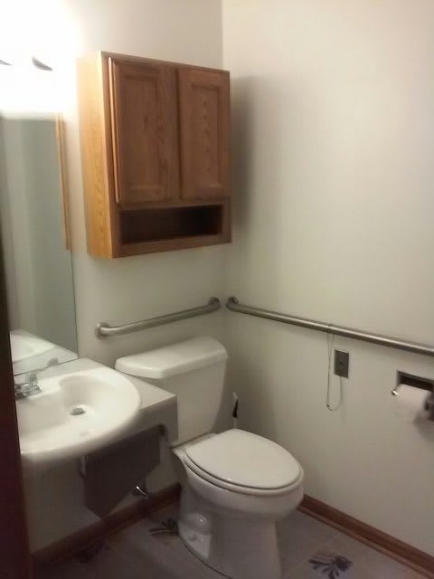 A small bathroom with a sink, toilet, and wooden cabinet.