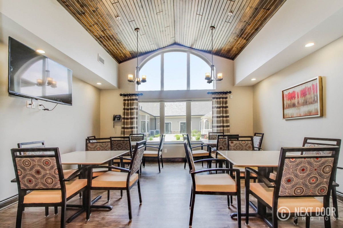 A spacious dining area with several tables and chairs, featuring a large window and wooden ceiling.