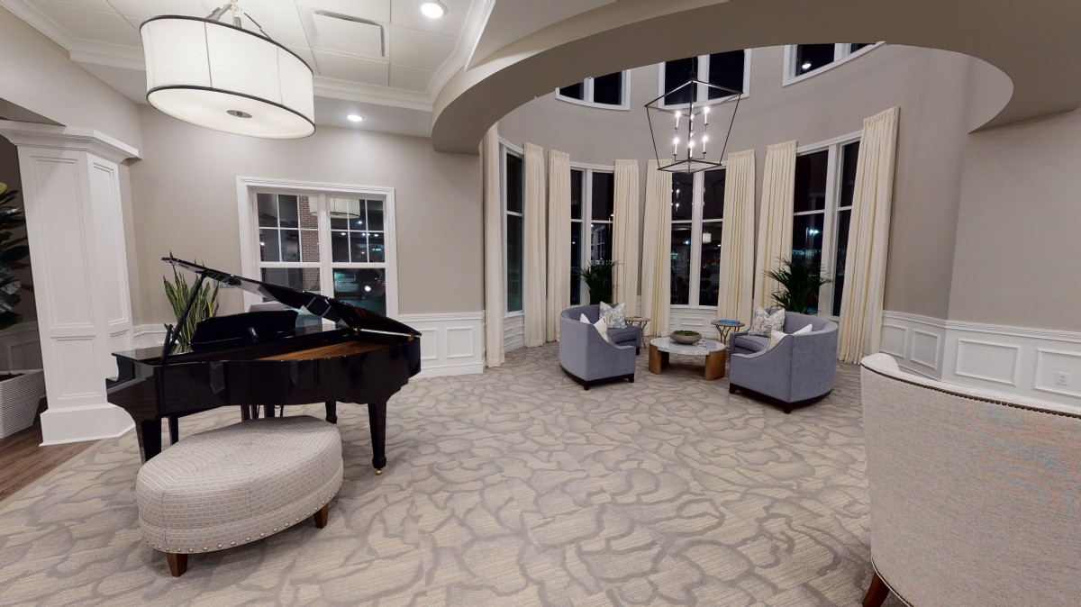 A spacious and elegant living room featuring a grand piano and comfortable seating with large windows offering ample natural light.