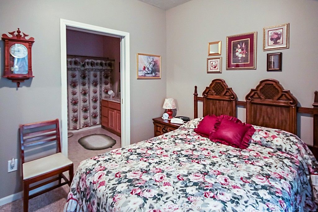 A cozy bedroom with floral bedding, wooden furniture, and a glimpse into an adjoining bathroom.