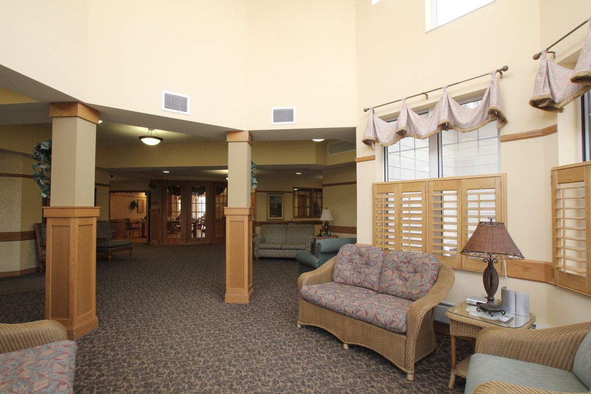A spacious lobby area with comfortable seating, featuring a sofa, carpeted floor, and large windows with curtains.