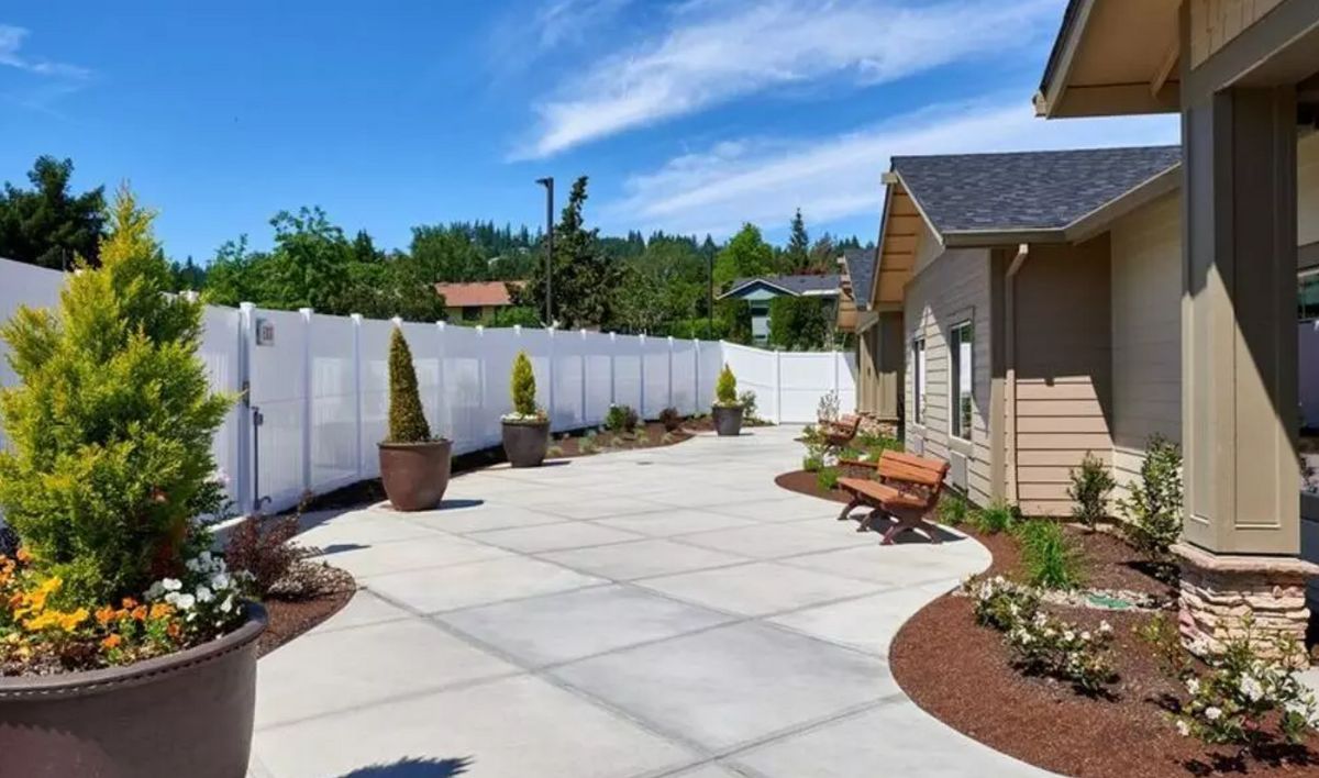 A spacious backyard patio with potted plants, benches, and a white fence under a clear blue sky.