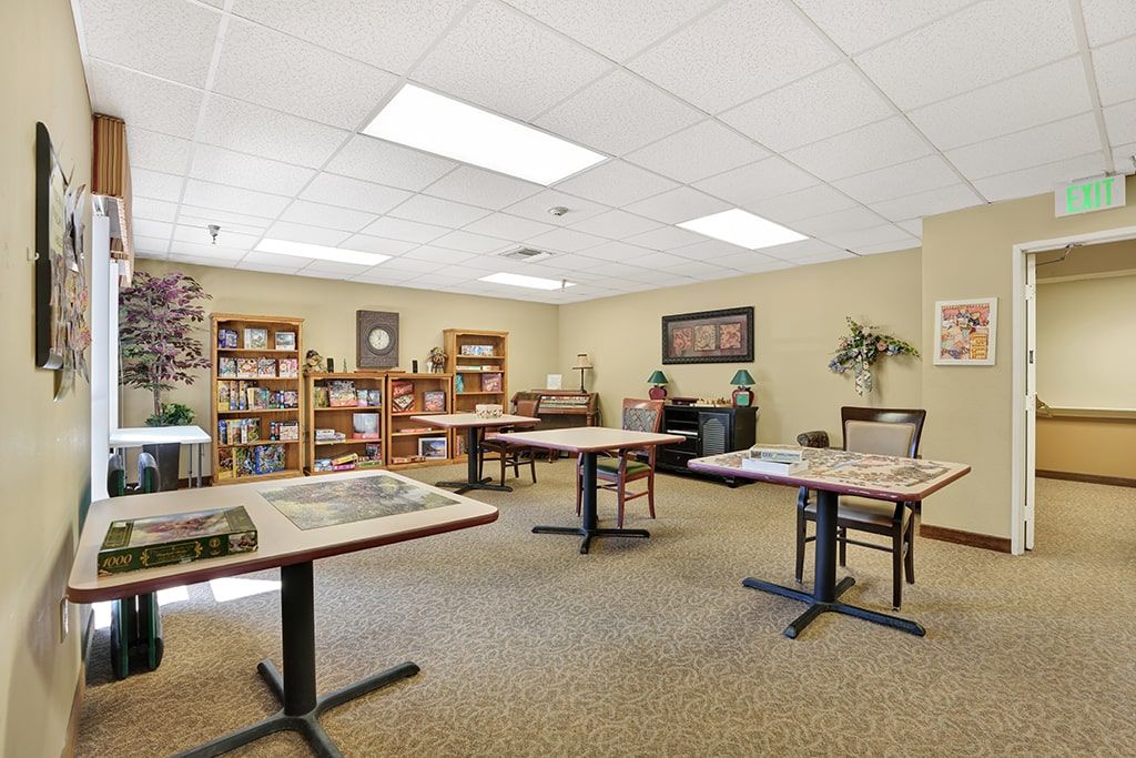 A library room with bookshelves, tables, and chairs under fluorescent lighting.