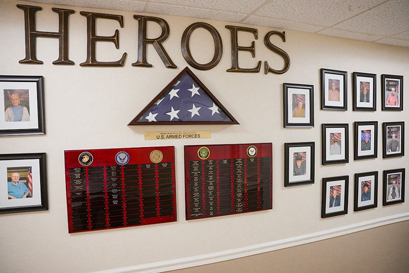 A memorial wall dedicated to heroes, featuring an American flag, plaques, and framed pictures.