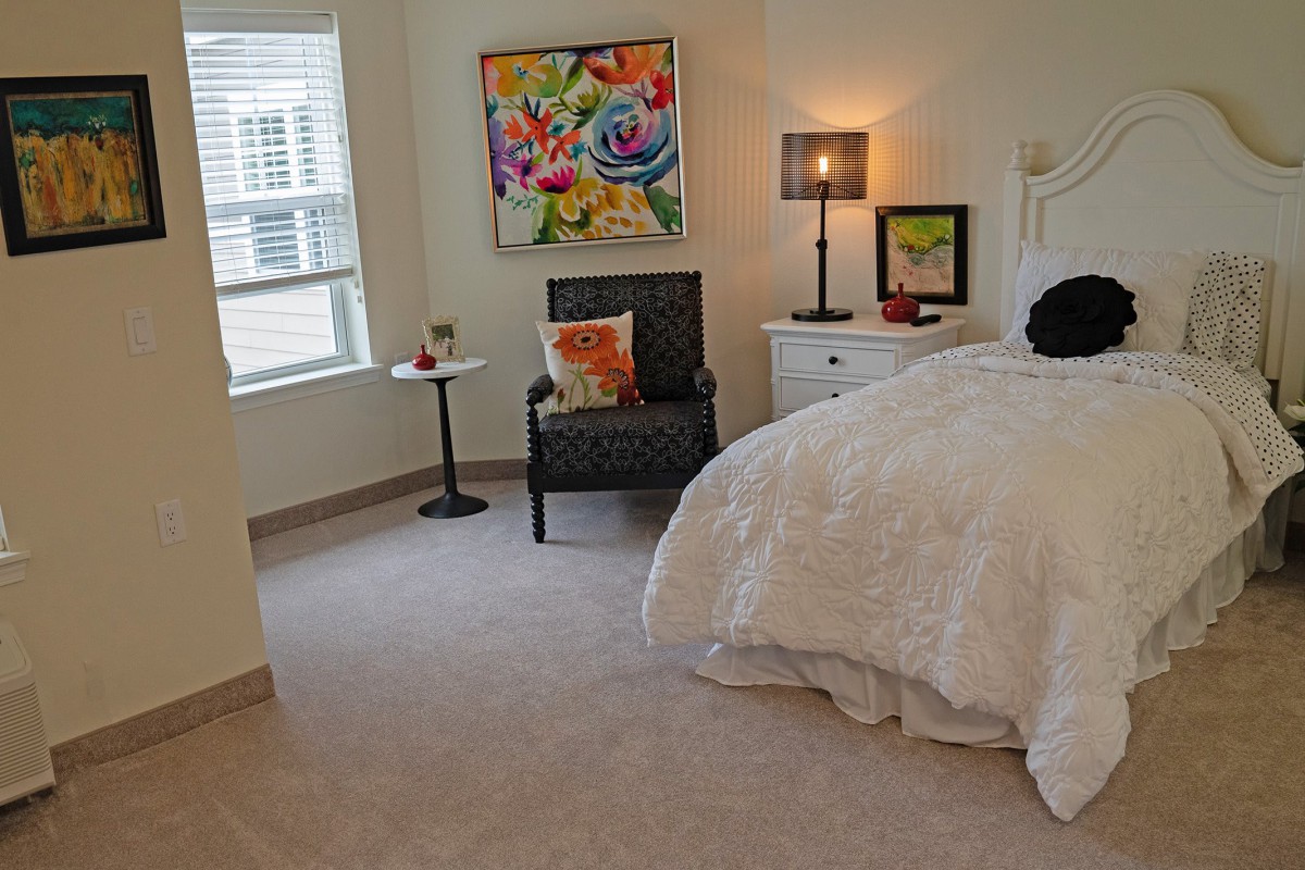 A cozy bedroom with a comfortable bed, decorative artwork, and a seating area with a lamp.