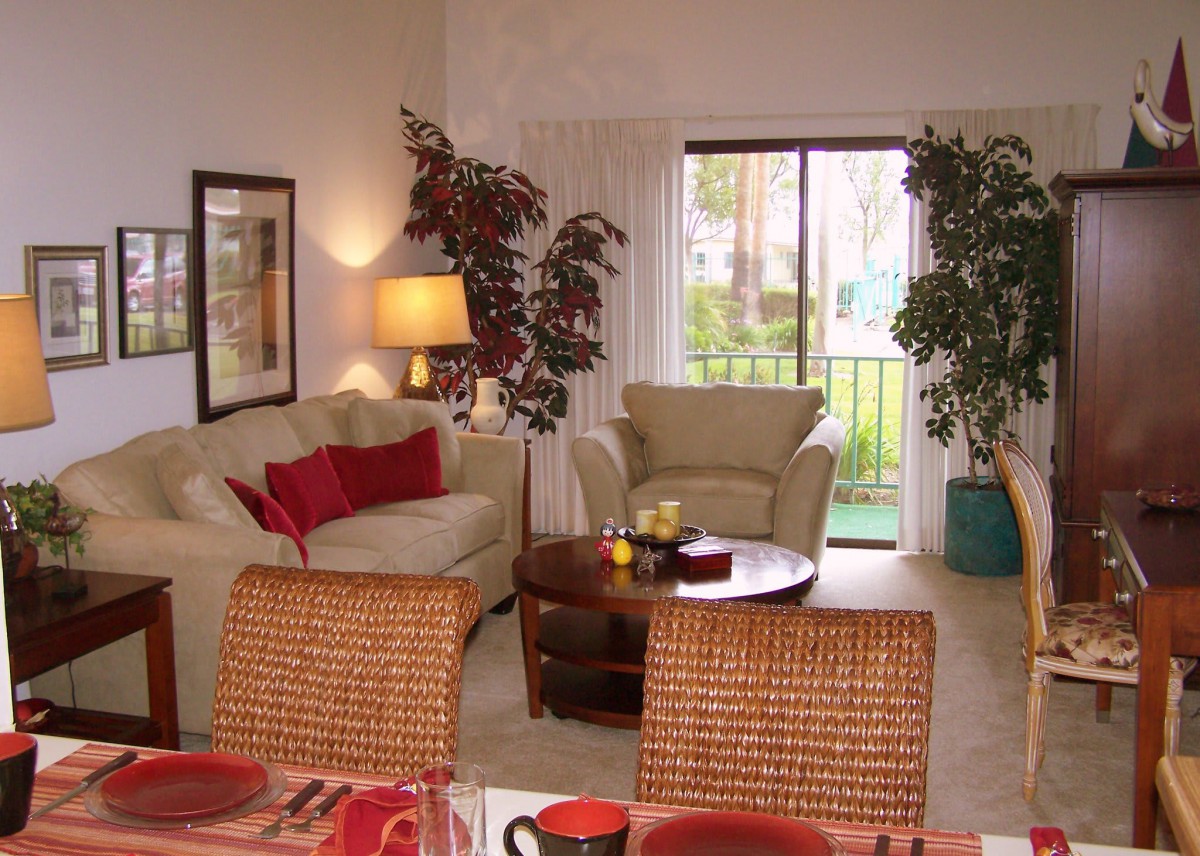 A cozy living room featuring comfortable sofas, a coffee table, and lush indoor plants, with a view of the outside through sliding glass doors.