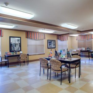 A well-lit room with tables and chairs, featuring decorated walls and a tiled floor.
