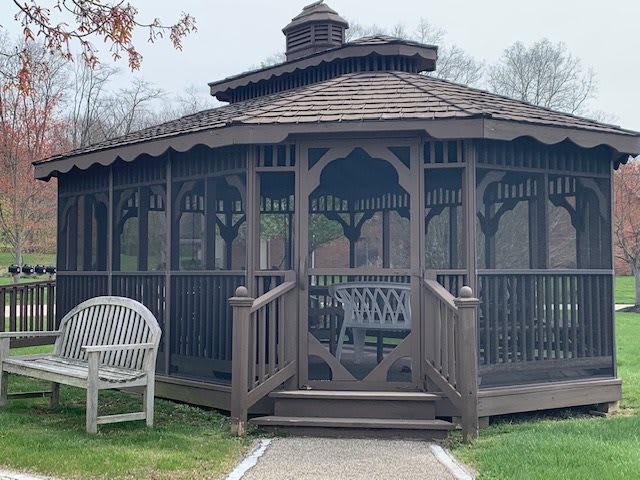 A wooden gazebo surrounded by greenery with a bench nearby.