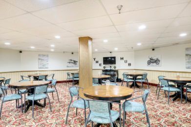 A neatly arranged dining area with round tables and chairs, featuring patterned carpet and wall decorations.
