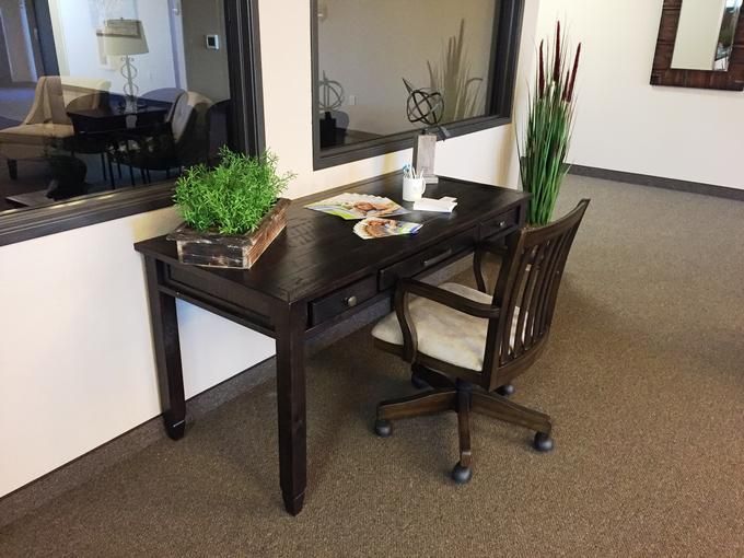 A neatly arranged office workspace with a dark wooden desk and chair, adorned with green plants for decoration.