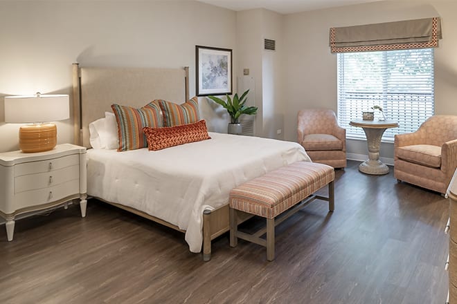 A modern bedroom with a neatly made bed, stylish armchair, and soft lighting.