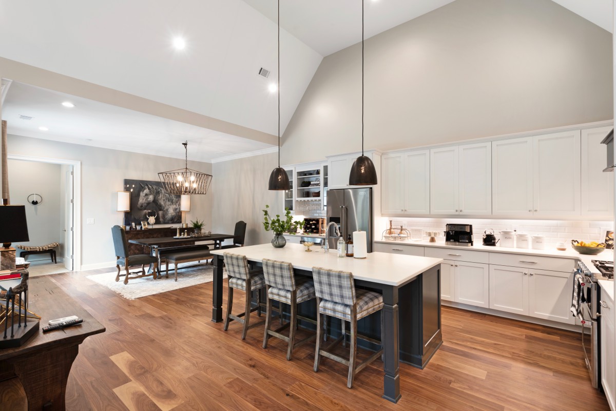 A modern open-concept kitchen with an island, hardwood floors, and pendant lighting next to a dining area.