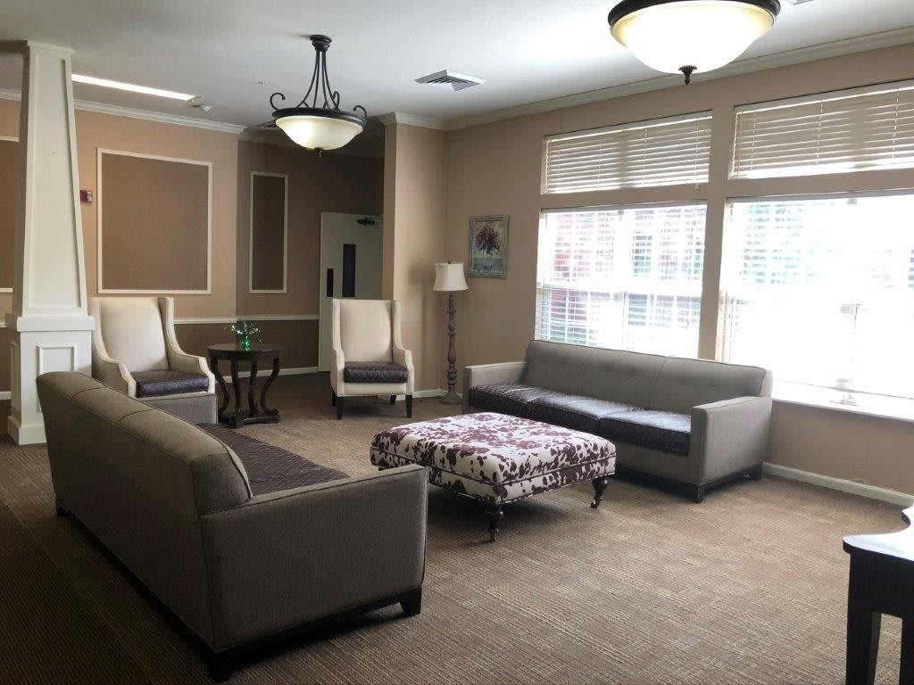 A cozy living room with sofas, armchairs, a patterned coffee table, and large windows letting in natural light.