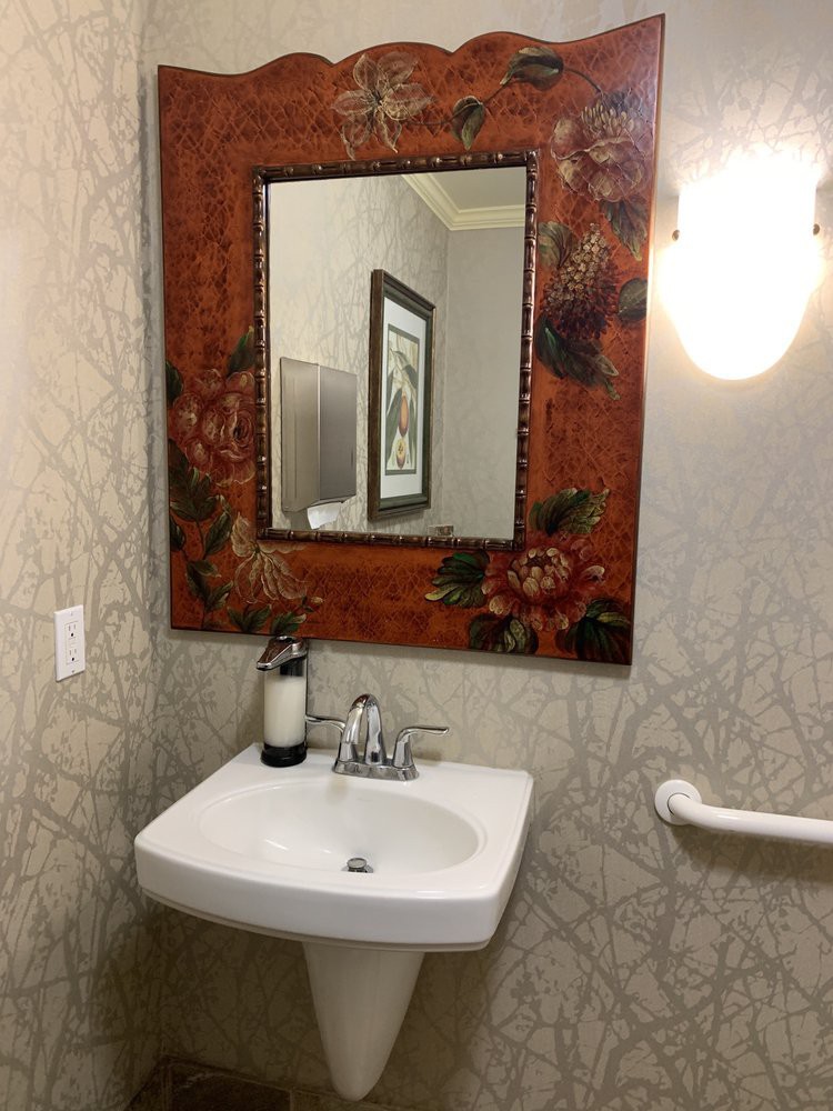 A small bathroom with a decorative mirror, sink, and light fixture.