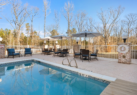 A serene outdoor swimming pool area featuring patio furniture and umbrellas under a clear blue sky.