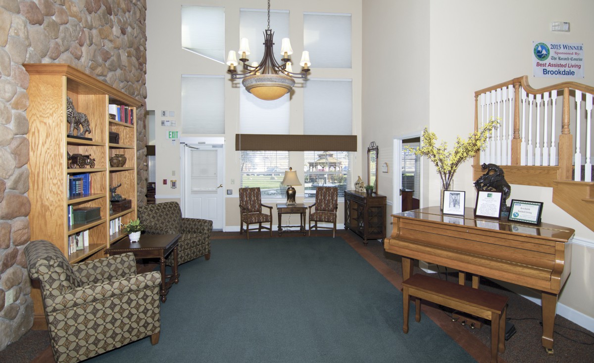 A spacious living room with a chandelier, piano, and comfortable seating arrangements.