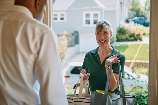 A friendly delivery person greets a customer at the door with a smile and bags in hand.