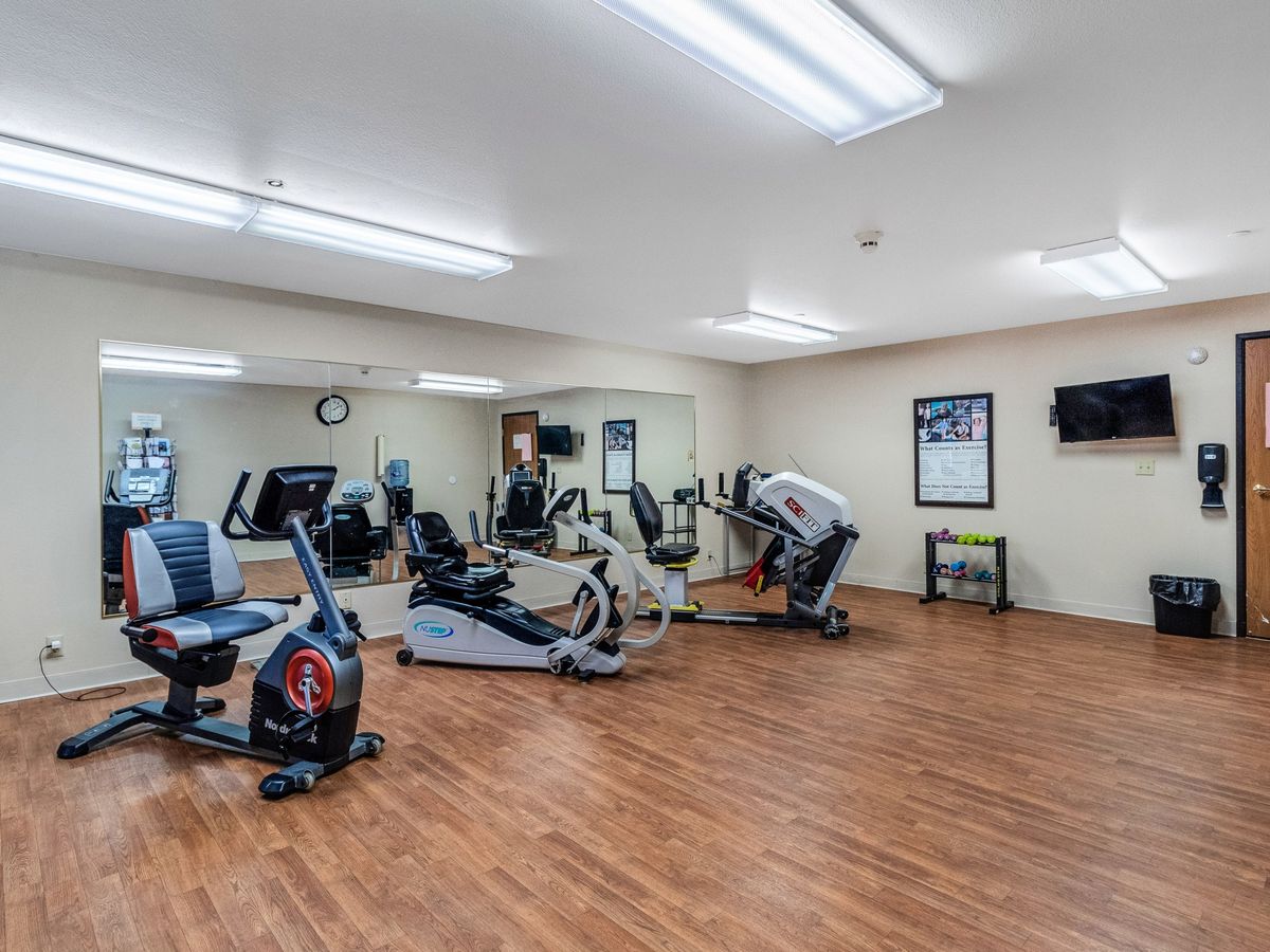 A well-lit fitness room with various exercise machines and wooden flooring.