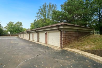 A row of brick garages along a paved driveway surrounded by trees.