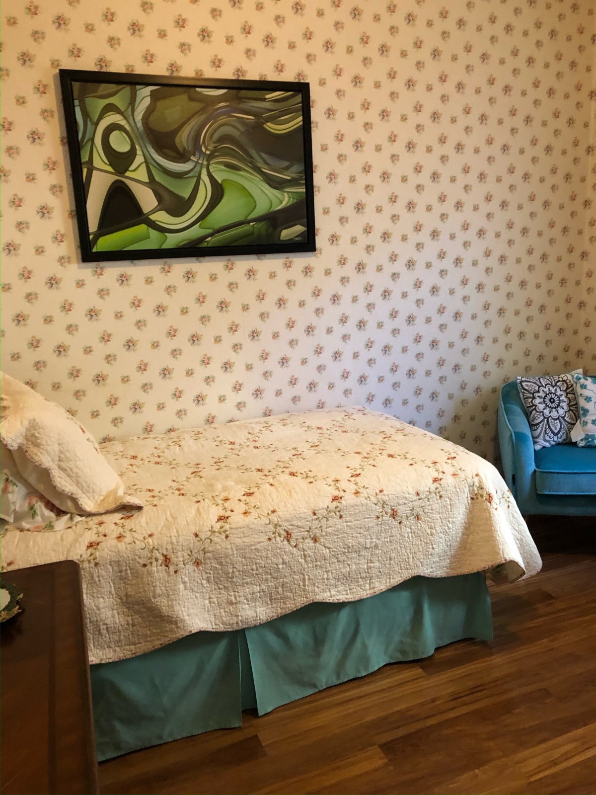 A cozy bedroom with a single bed, decorative wallpaper, and colorful artwork.