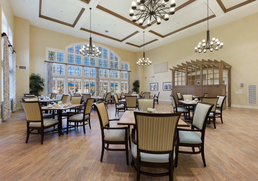 A spacious and elegantly designed dining room with multiple tables and chairs, featuring large windows and stylish chandeliers.