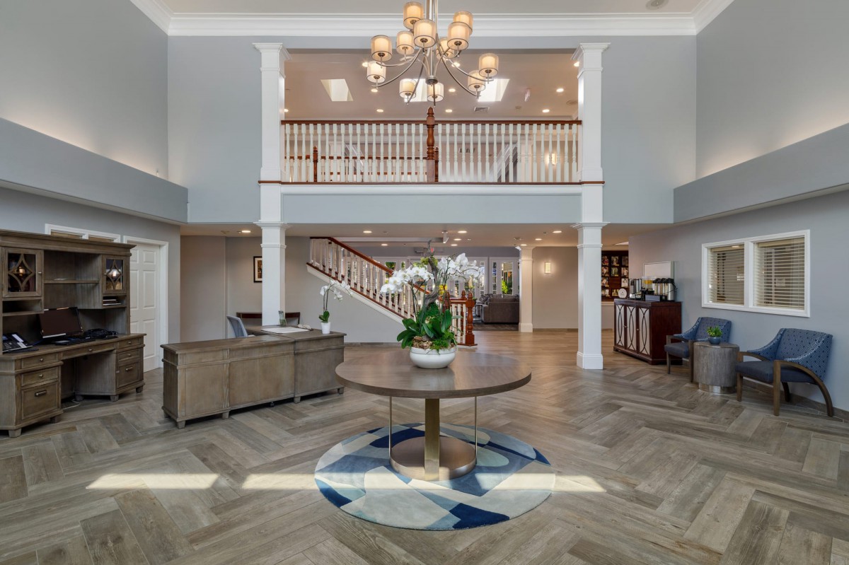 A spacious and elegantly decorated lobby with a chandelier and central staircase.