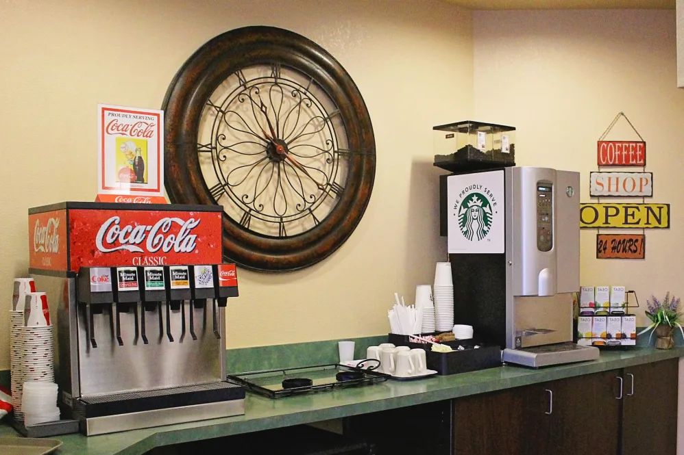 Beverage station with a soda fountain, Starbucks coffee machine, and a wall clock.