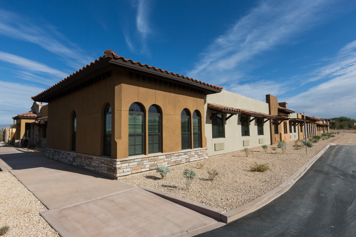 A southwestern-style home with stucco walls, arched windows, and xeriscape landscaping under a clear blue sky.