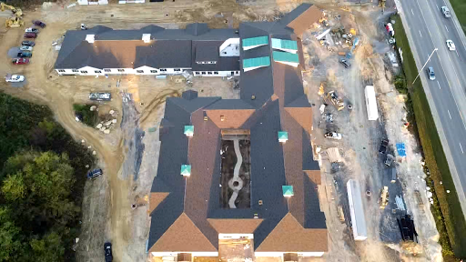 An aerial view of a building under construction, showcasing the roof layout and surrounding site.