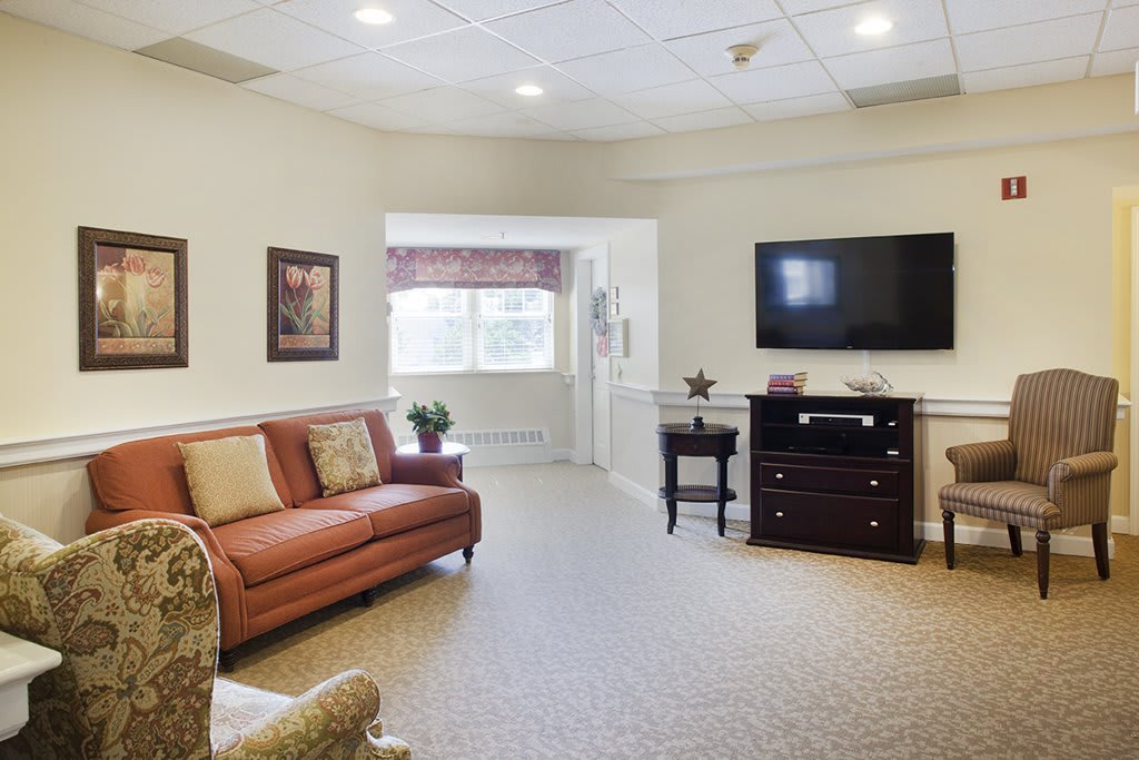 A cozy living room with a sofa, armchair, and a wall-mounted television.