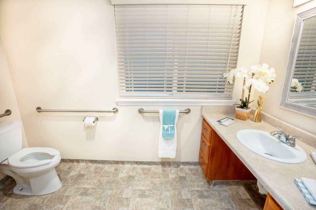 A clean and spacious bathroom with a sink, toilet, towel rack, and window blinds.