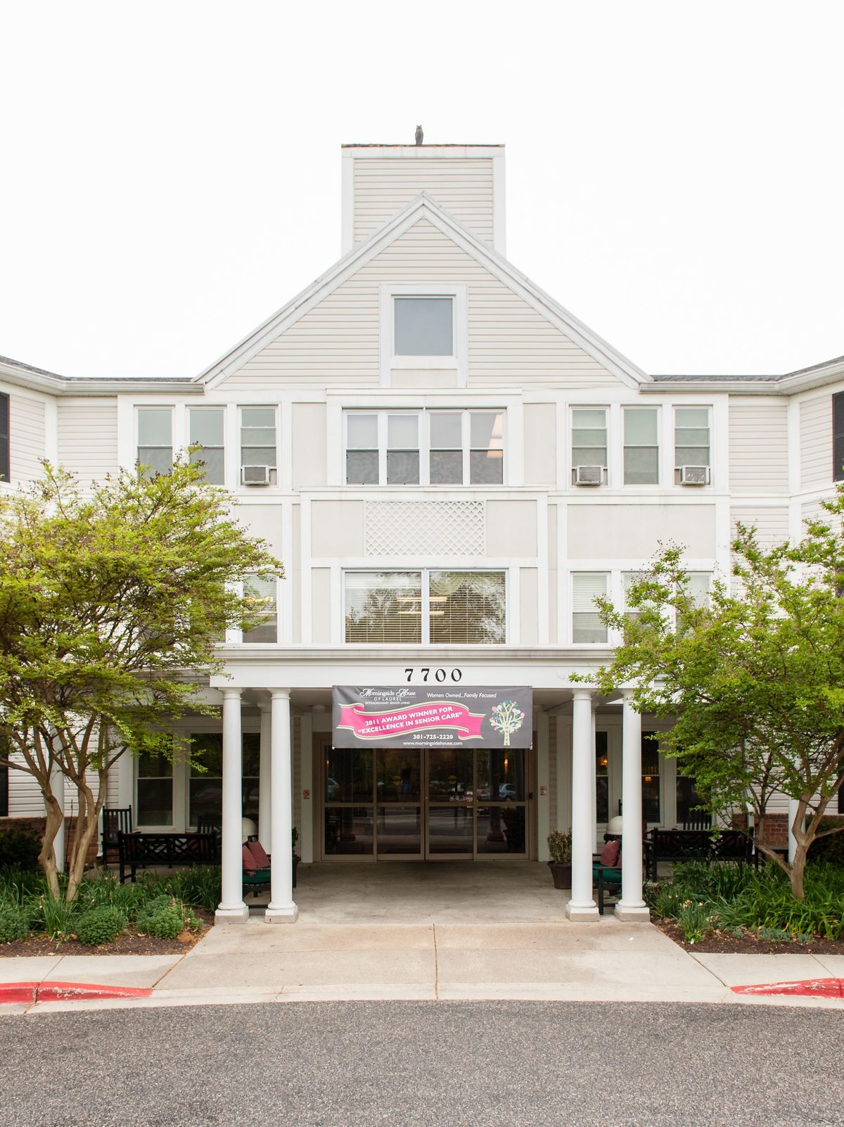 The entrance of a white building with columns and surrounding trees.