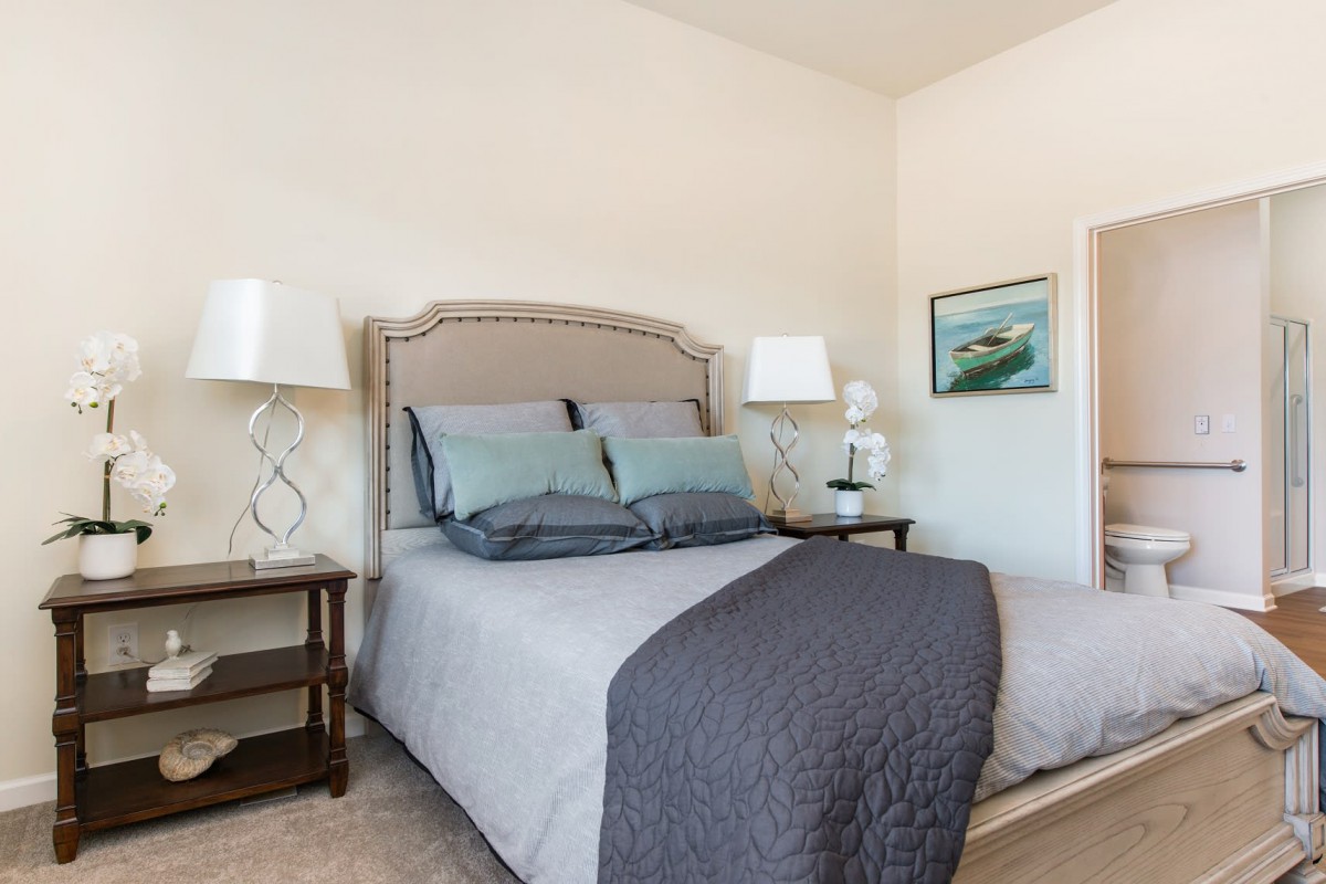 A cozy bedroom with a neatly made bed, nightstands, and lamps, accented by artwork on the wall.