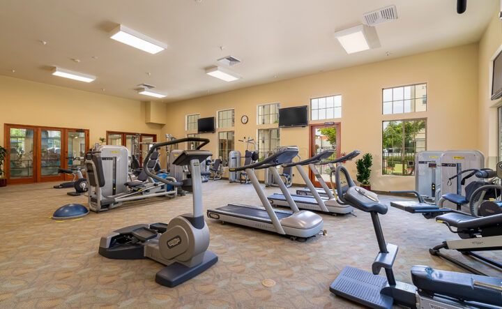 A well-equipped gym with various exercise machines and ample natural light.