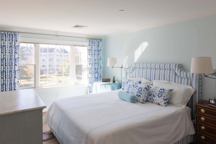 A bright and cozy bedroom with a light blue color scheme, featuring a bed adorned with decorative pillows and plenty of natural sunlight.