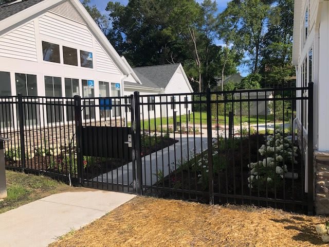 A residential house with a black metal fence and gate, featuring a concrete pathway leading to the entrance.