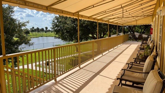 A sunny balcony with seating overlooking a lake and trees, sheltered by an awning.