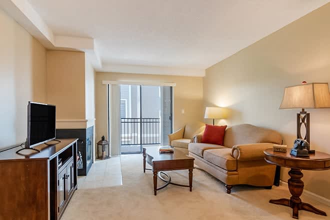 A cozy living room with a sofa, coffee table, and TV, leading to a balcony.