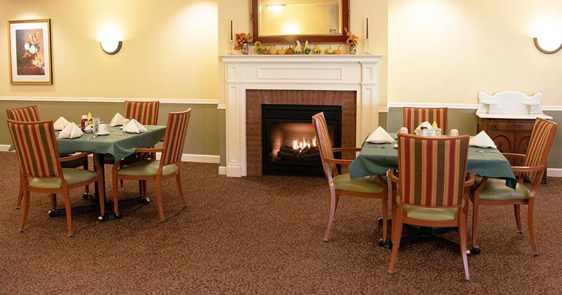 A cozy dining area featuring a lit fireplace and neatly arranged tables with chairs.