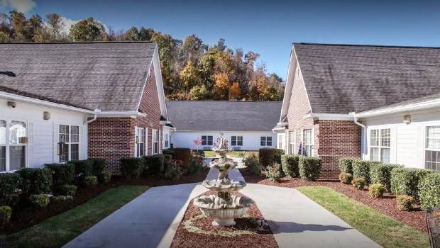 A quaint courtyard flanked by brick residential buildings, featuring a central fountain and surrounded by lush autumn foliage.