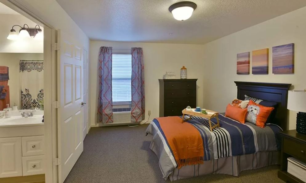 A cozy bedroom with a bed, dresser, and window covered by curtains.