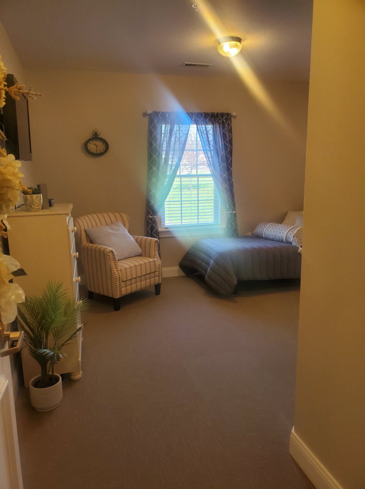 A cozy bedroom with a single bed, an armchair, and a window letting in natural light.