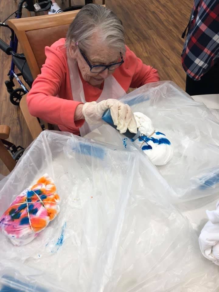 An elderly person engages in a colorful tie-dye project, mixing vibrant colors on fabric.
