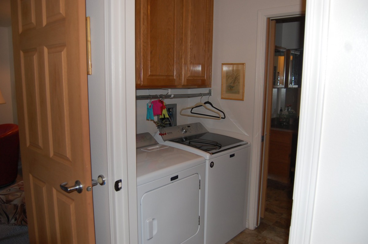A small laundry room with a washer and dryer placed side by side, featuring wooden cabinets above them.