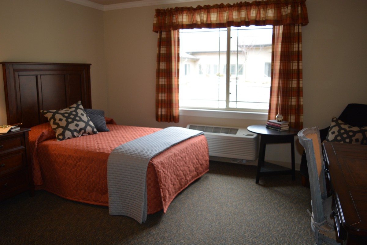 A cozy bedroom with an orange-themed decor, featuring a bed, bedside table, and a window with plaid curtains.