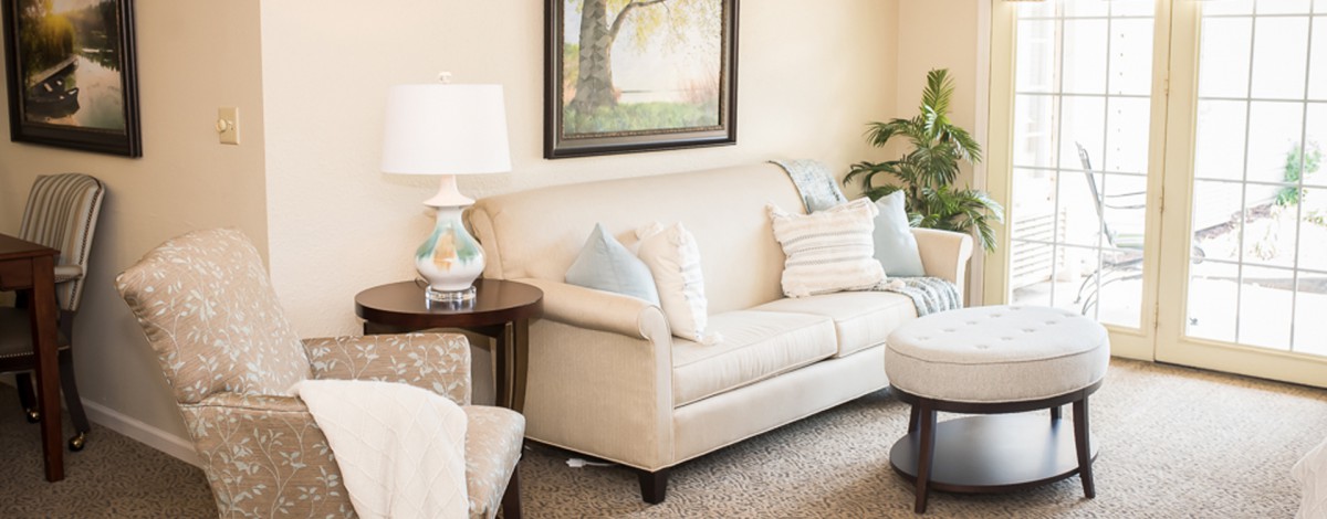 A cozy living room with a beige sofa, decorative pillows, a side lamp, and wall art.