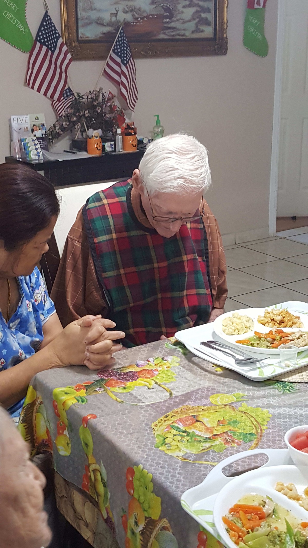 An elderly person and a caregiver sitting together at a dining table, engaged in conversation during a meal.