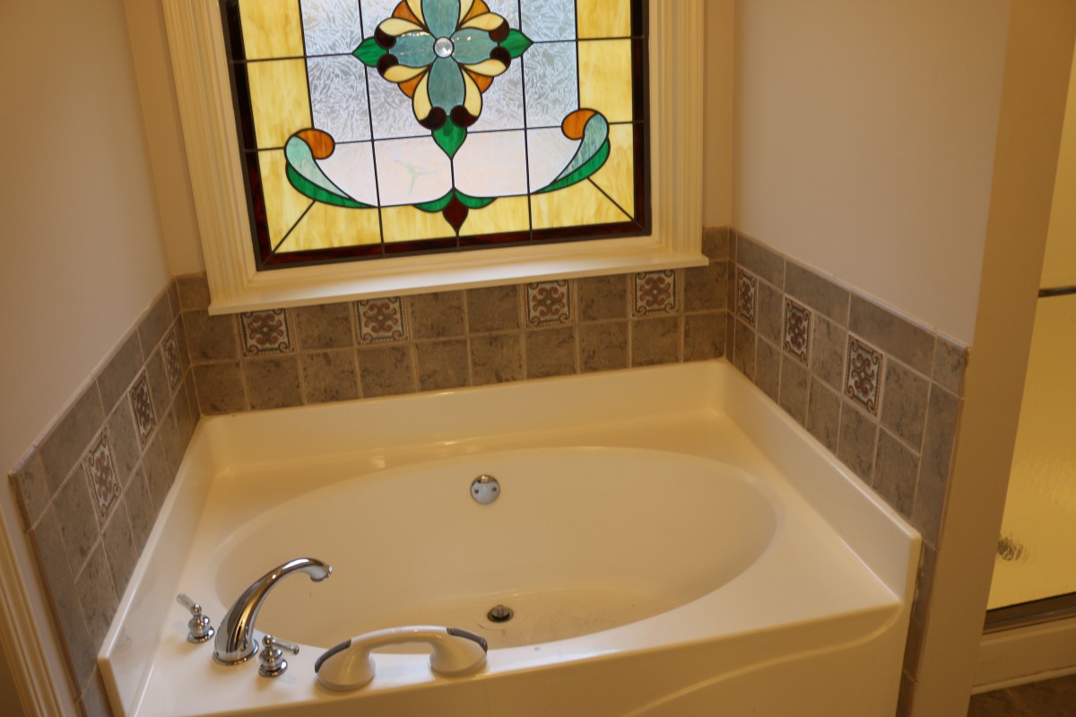 A cozy bathroom featuring a bathtub and a stained glass window.