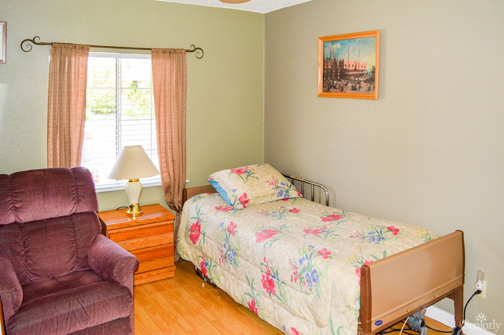 A cozy bedroom with a single bed featuring floral bedding, a bedside lamp, and curtains by the window.